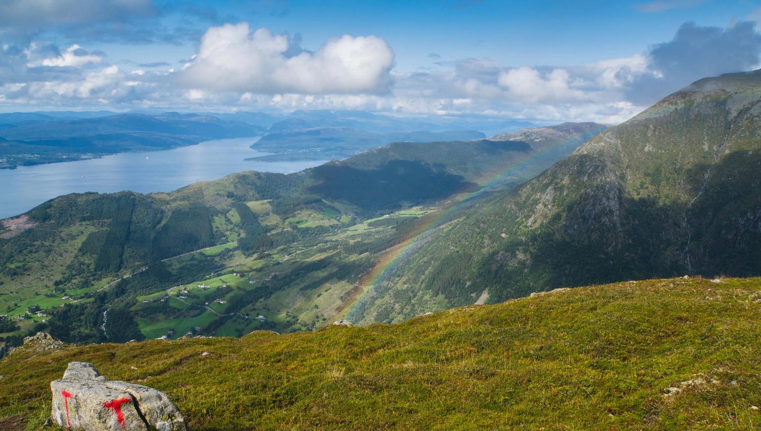 Fargerik regnboge som strekkjer seg over fjellsida ved Malmangernuten med utsyn mot Hardangerfjorden.