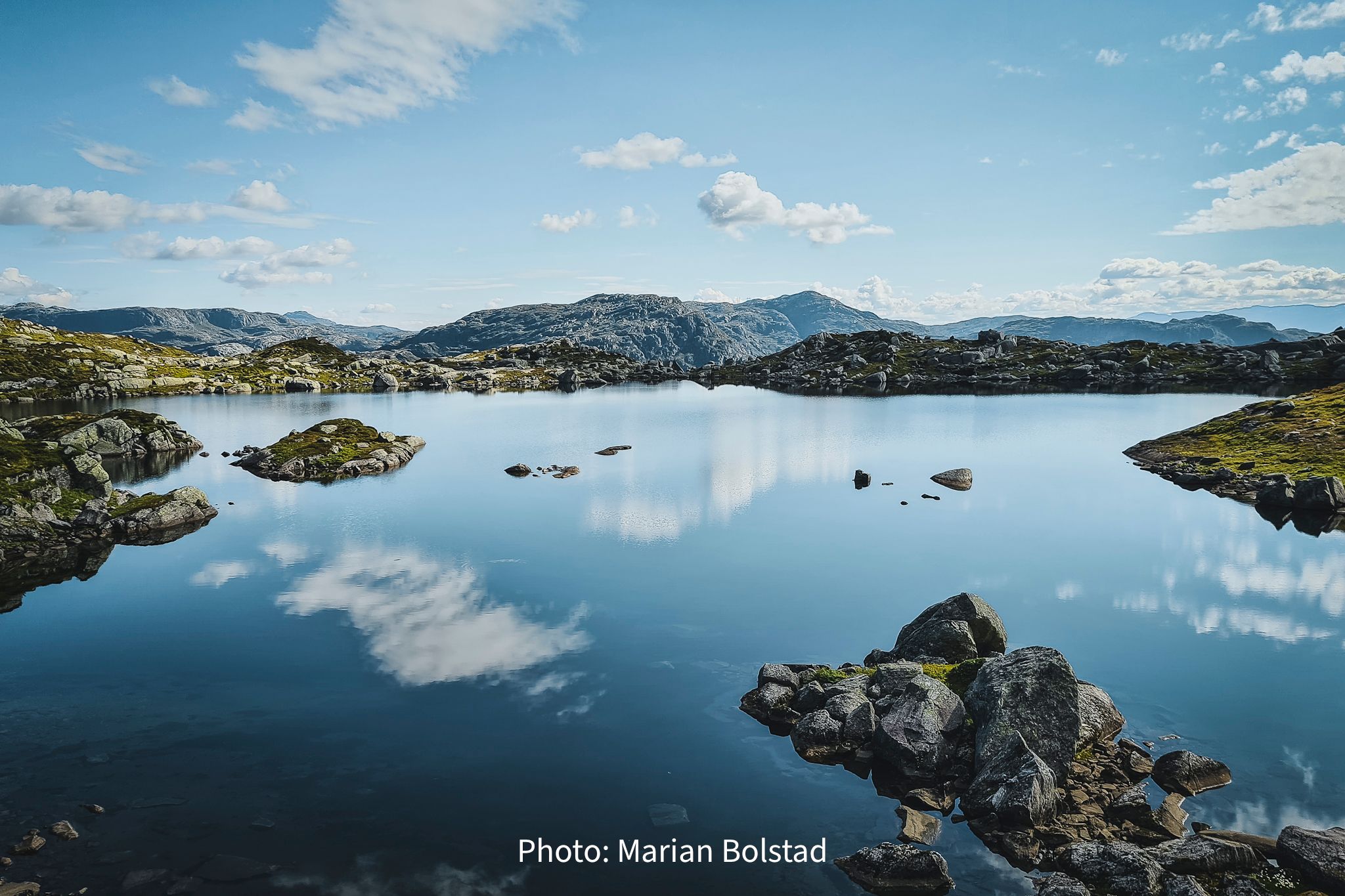 Calm mountain lake in Hardanger, Norway, reflecting sky and peaks in peaceful surroundings