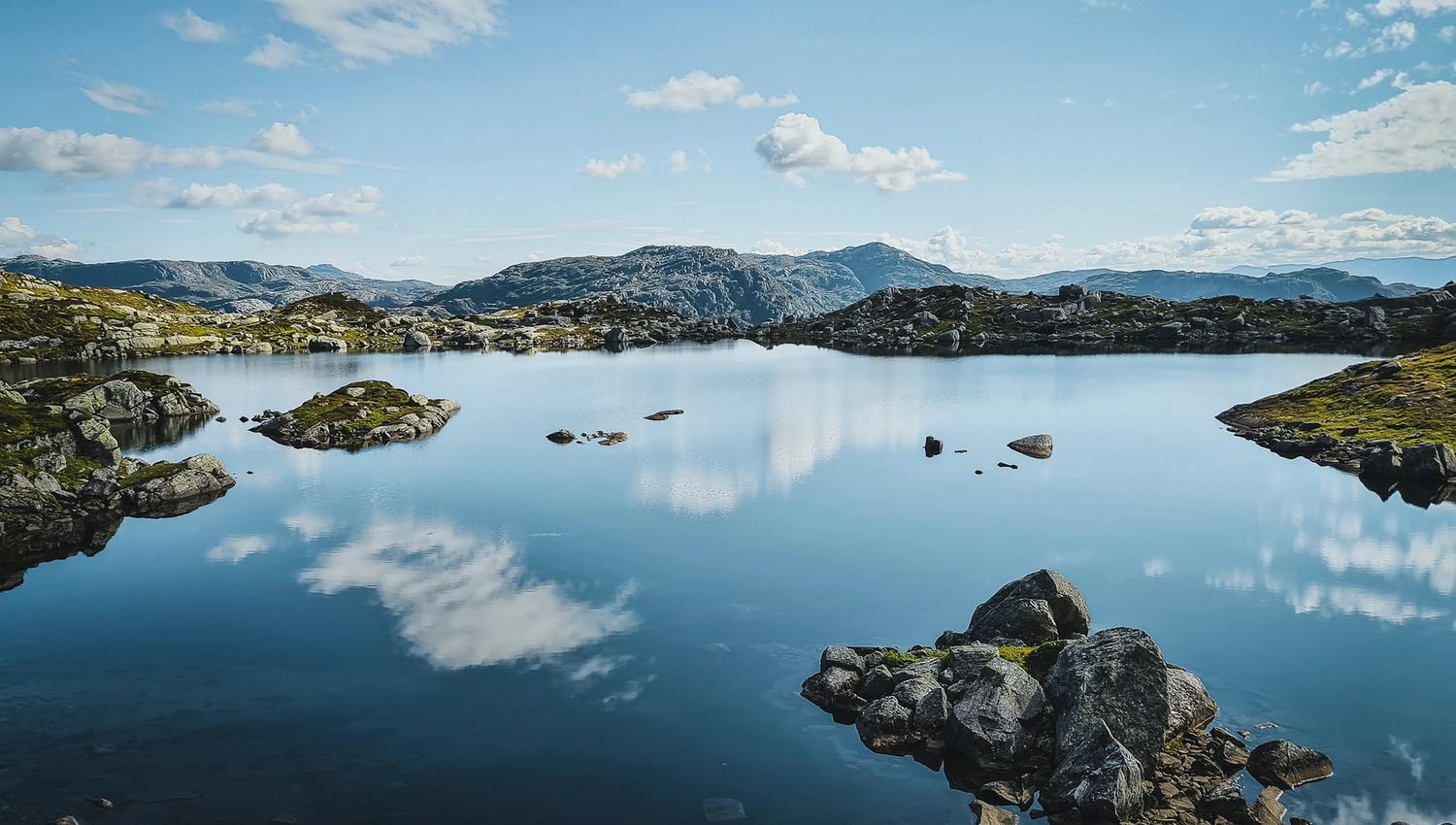 Calm mountain lake in Hardanger, Norway, reflecting sky and peaks in peaceful surroundings