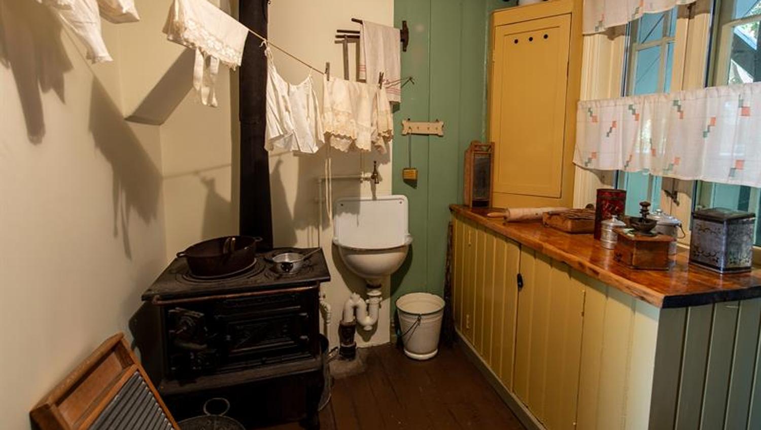 Reconstructed kitchen interior with a wood-burning stove, drying laundry and historic kitchen utensils from an older workers’ home.
