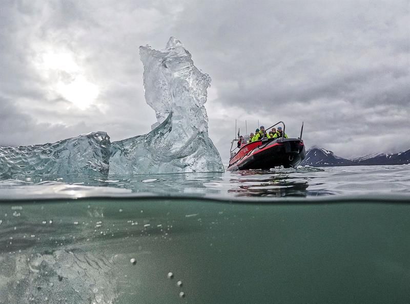 Split-level view of an iceberg with a RIB boat nearby in overcast weather.