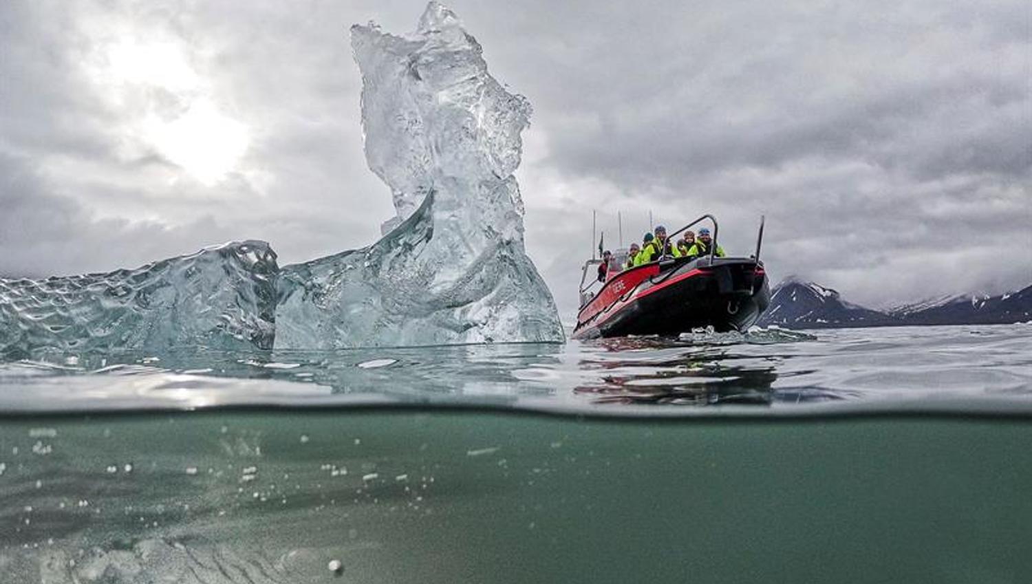 Split-level view of an iceberg with a RIB boat nearby in overcast weather.