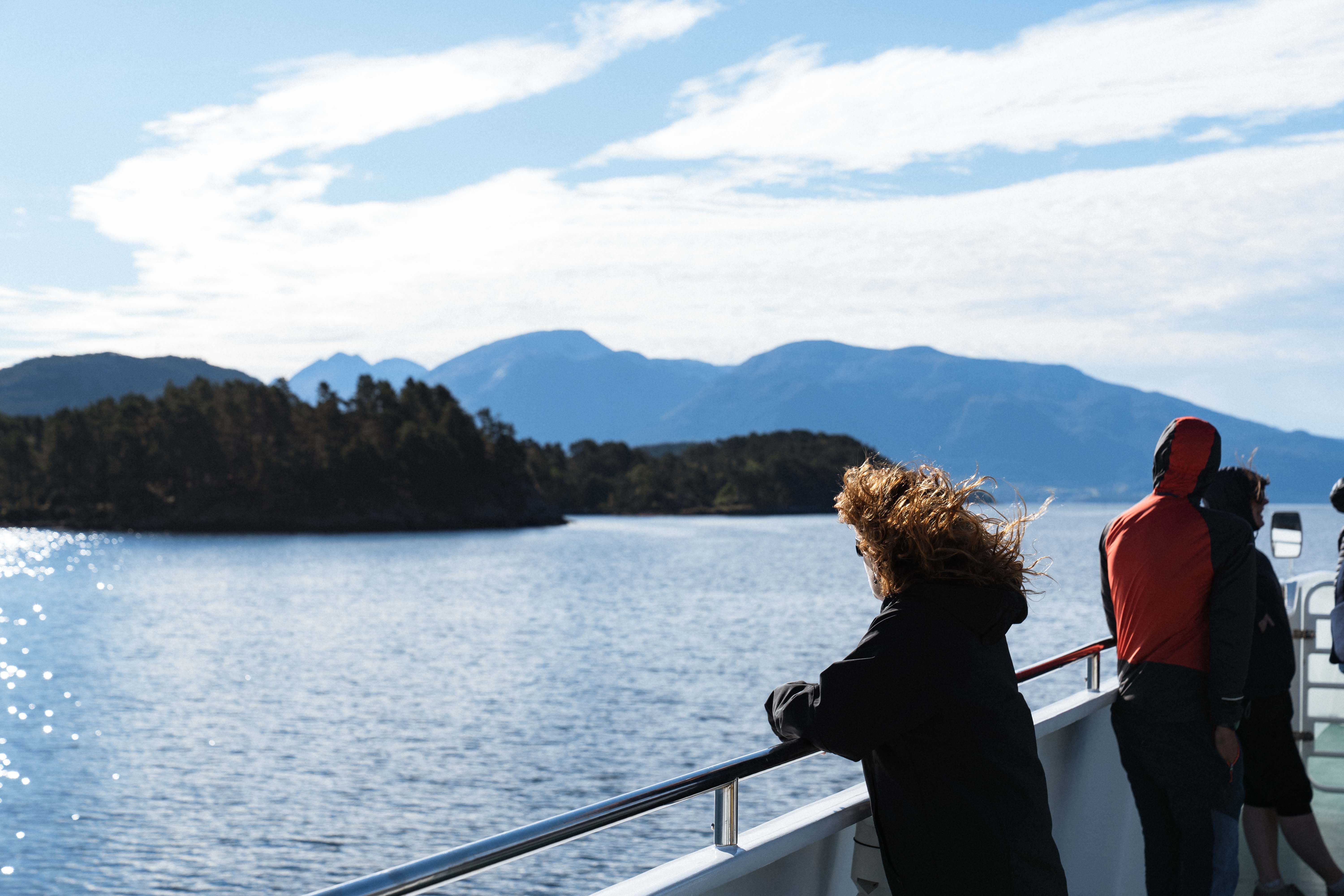 A woman gazing over the fjord and mountain landscape from Hardangerfjordekspressen in the fresh air.