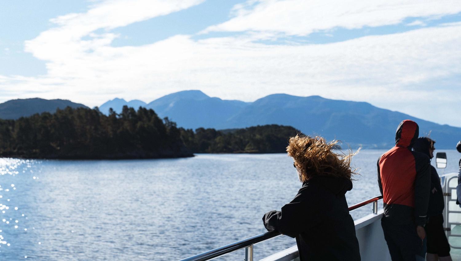 A woman gazing over the fjord and mountain landscape from Hardangerfjordekspressen in the fresh air.