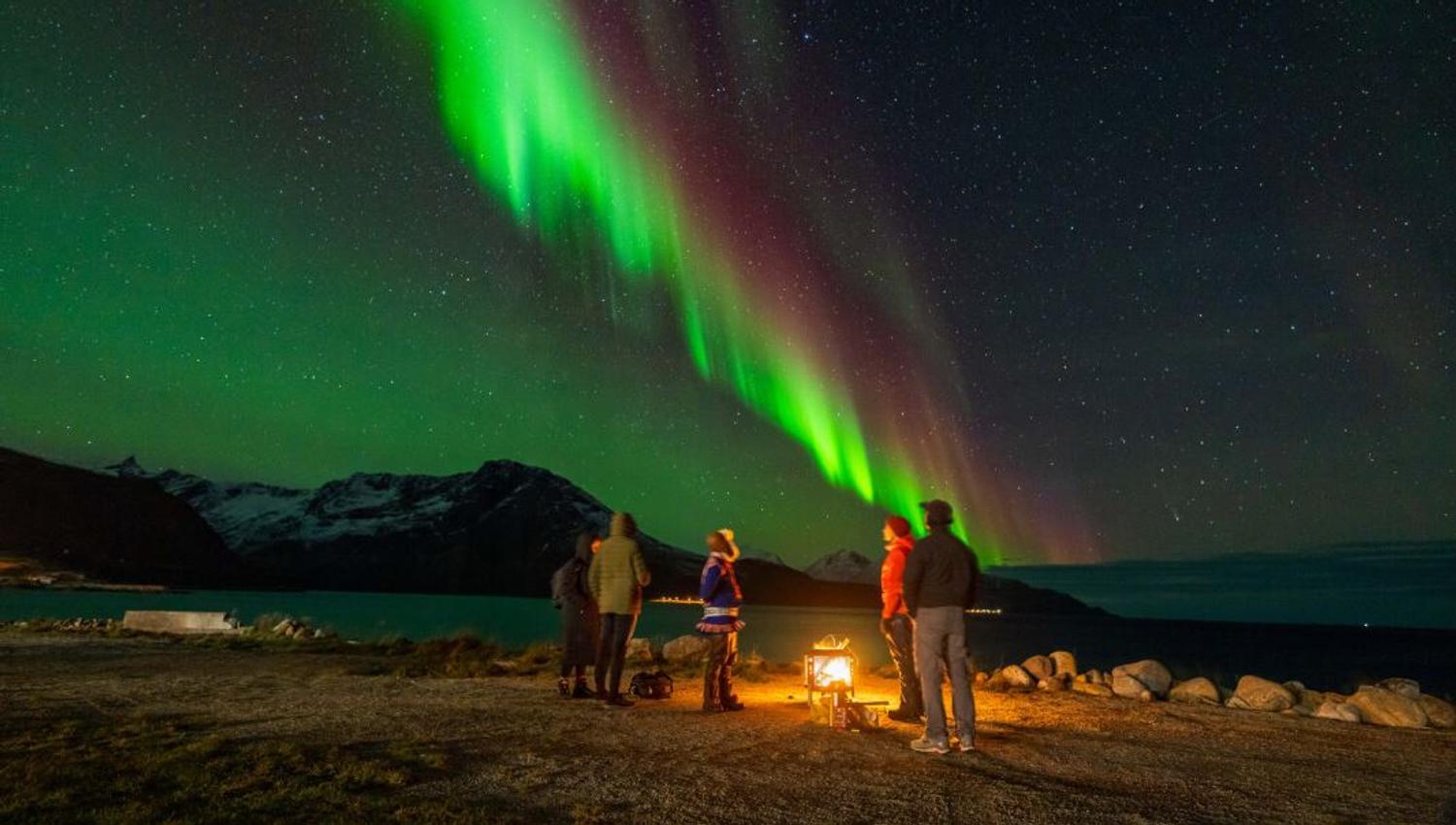 Guests sit around the fire, watching the Northern Lights dance overhead