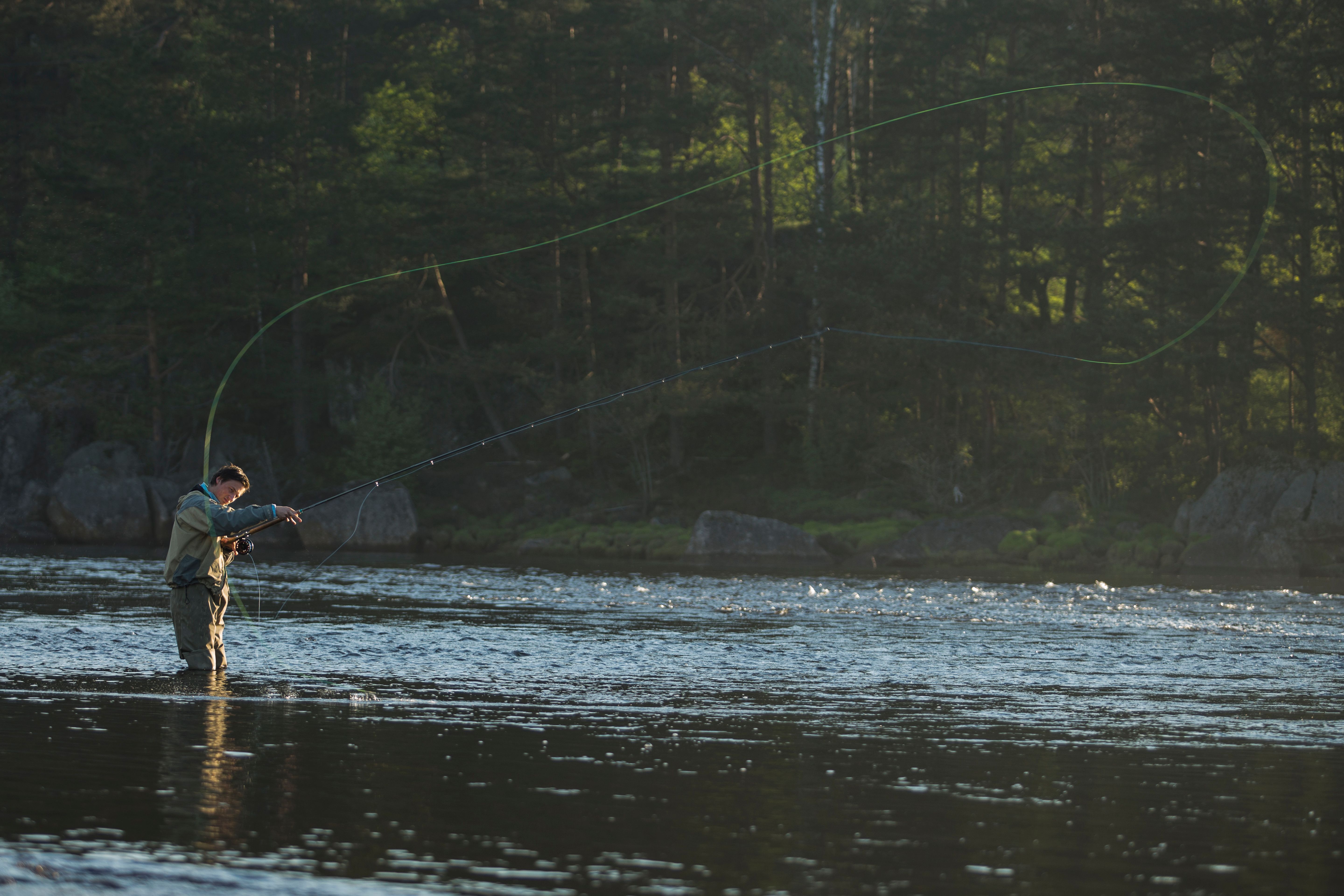A man in waders standing knee-deep in the water, fly fishing