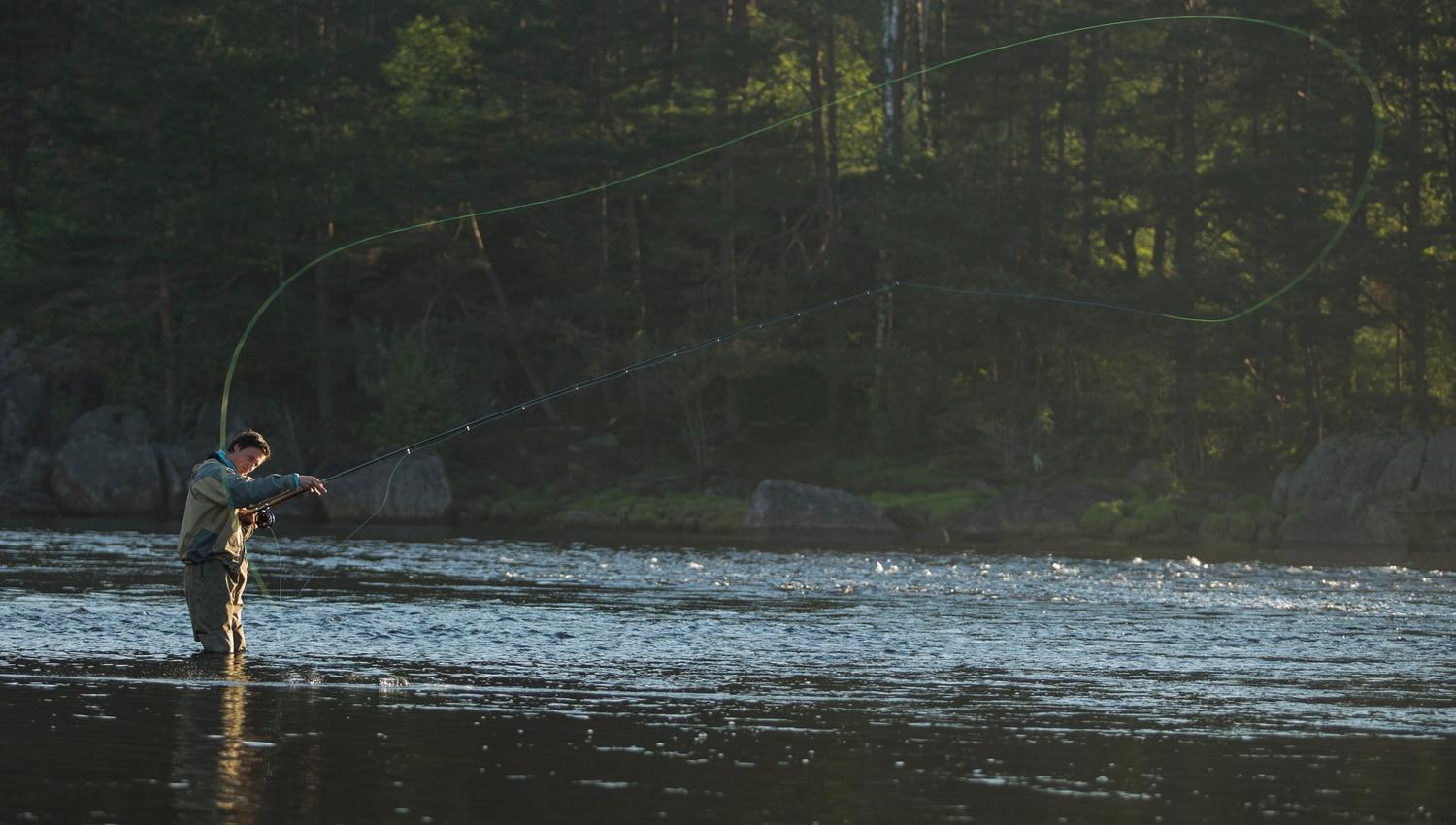 A man in waders standing knee-deep in the water, fly fishing