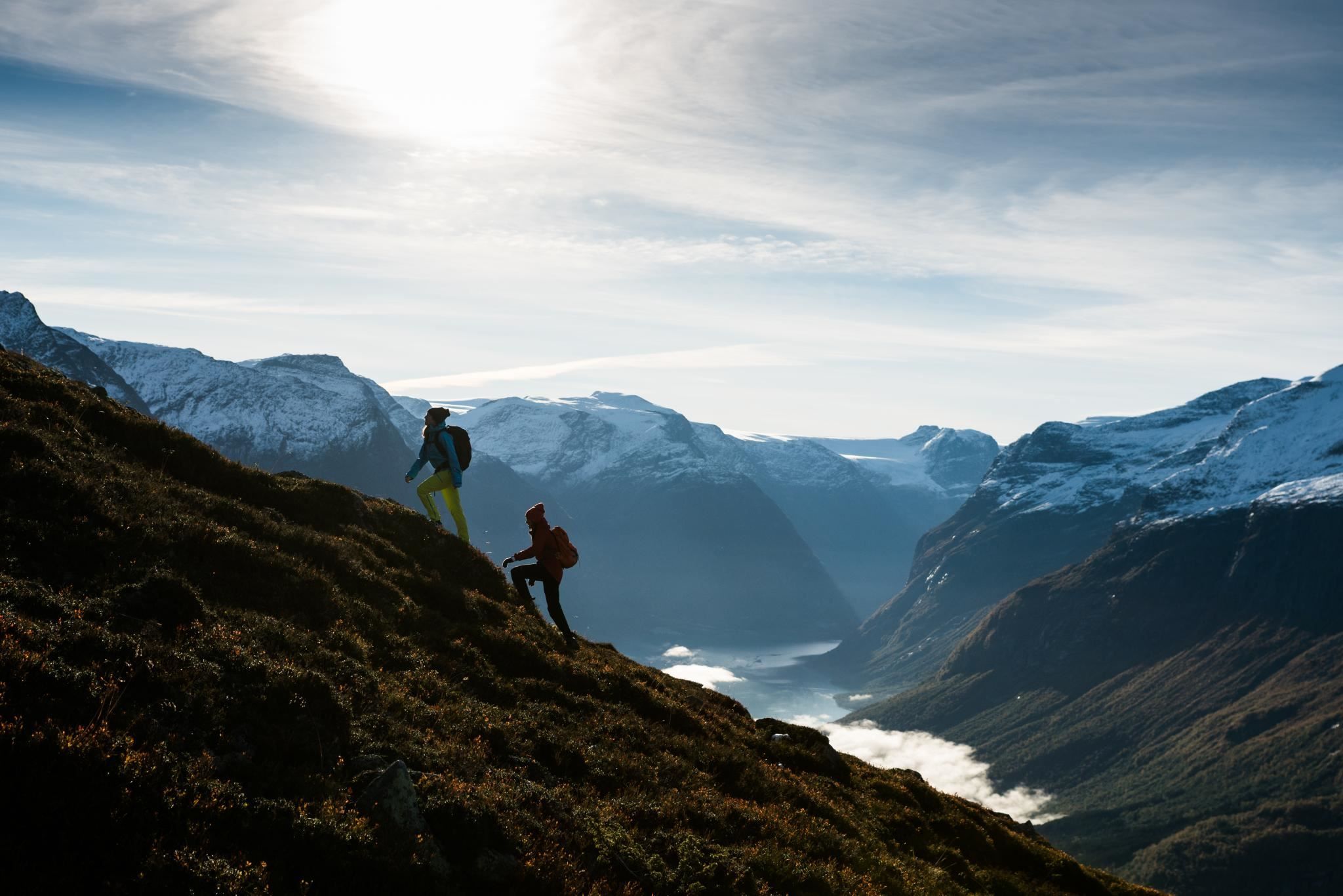 Hikers following a mountain trail at Hoven with views towards the fjord and surrounding peaks.