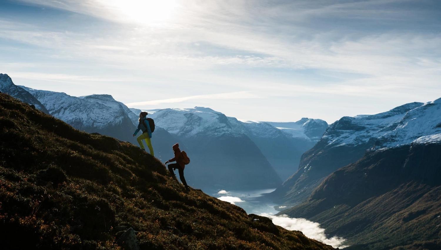 Hikers following a mountain trail at Hoven with views towards the fjord and surrounding peaks.