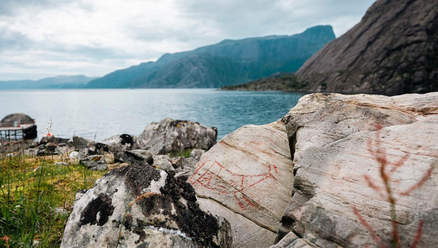 Ancient rock carvings in the Vingen rock art landscape, with the fjord and mountains in the background.