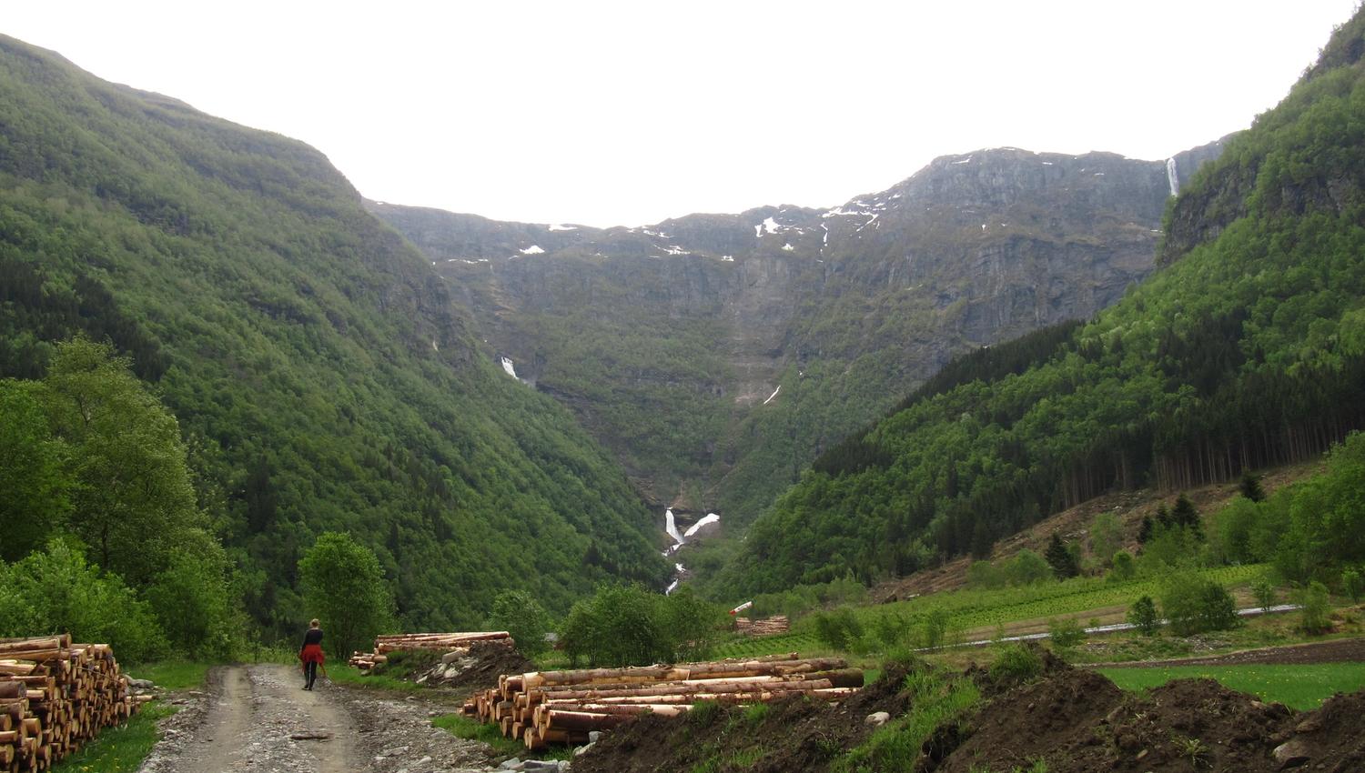 Hiking along a gravel road through a green valley with a distant waterfall in Elvedalen, Lofthus.