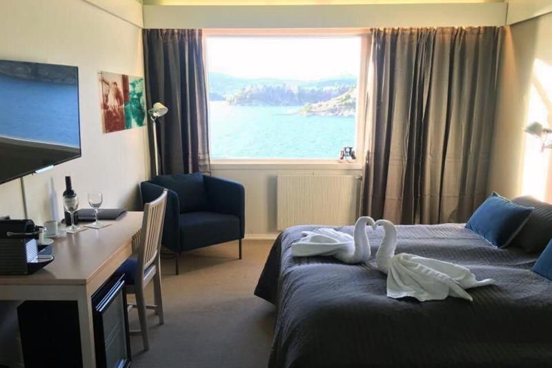 dobbeltrom med seng, skrivebord, lenestol, tv, håndkle-svaner og utsikt over fjorden