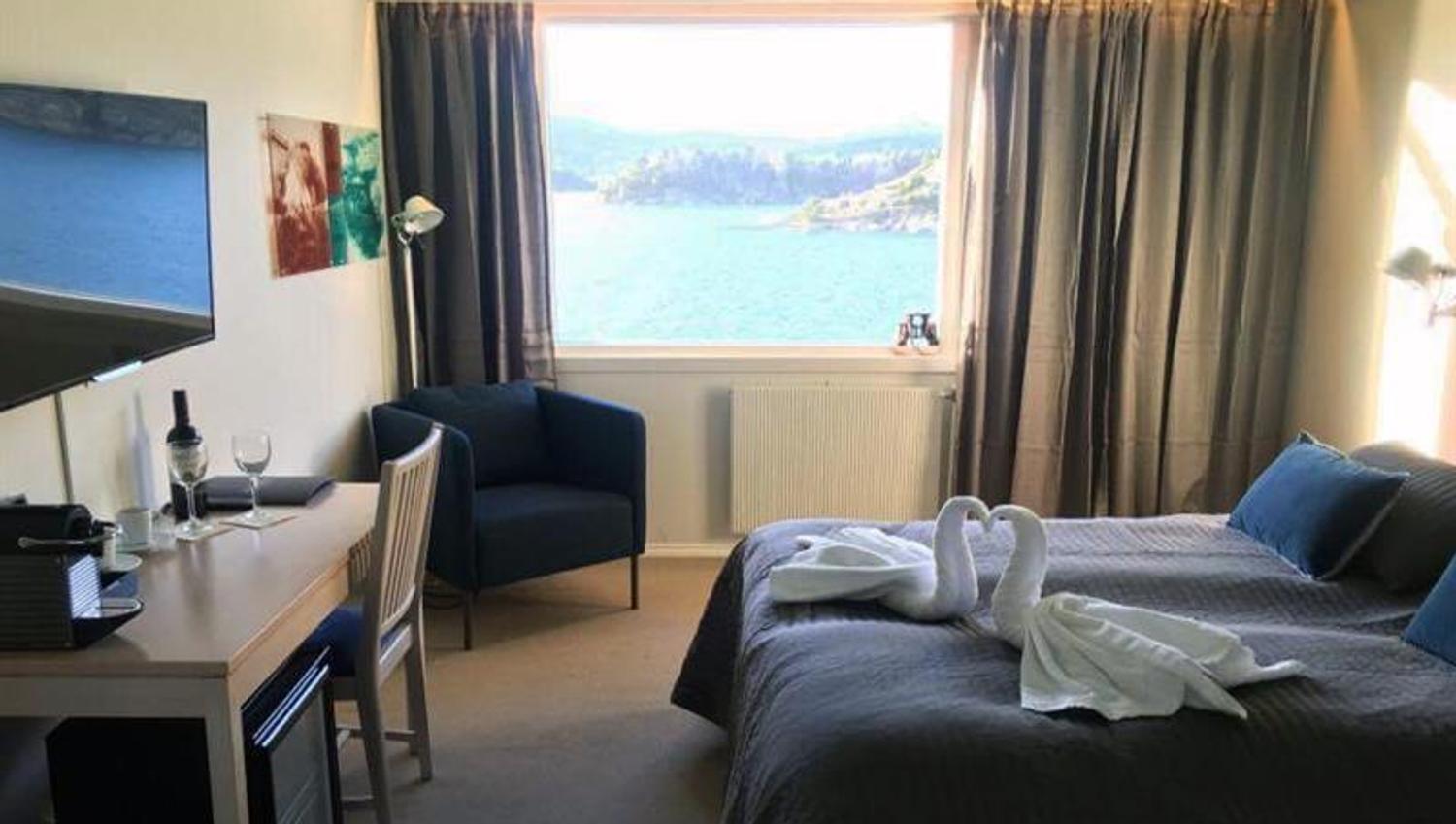 dobbeltrom med seng, skrivebord, lenestol, tv, håndkle-svaner og utsikt over fjorden