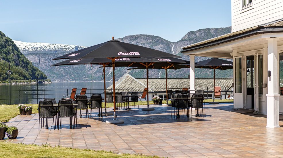 The outside patio with tables, chairs and parasols. The fjord seen in the background.