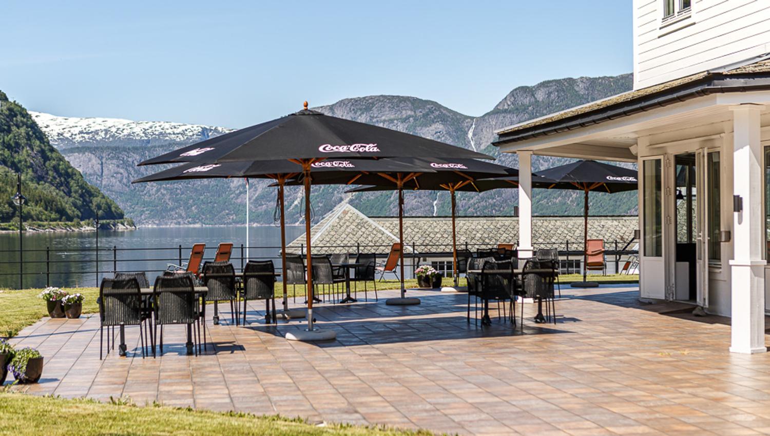 The outside patio with tables, chairs and parasols. The fjord seen in the background.