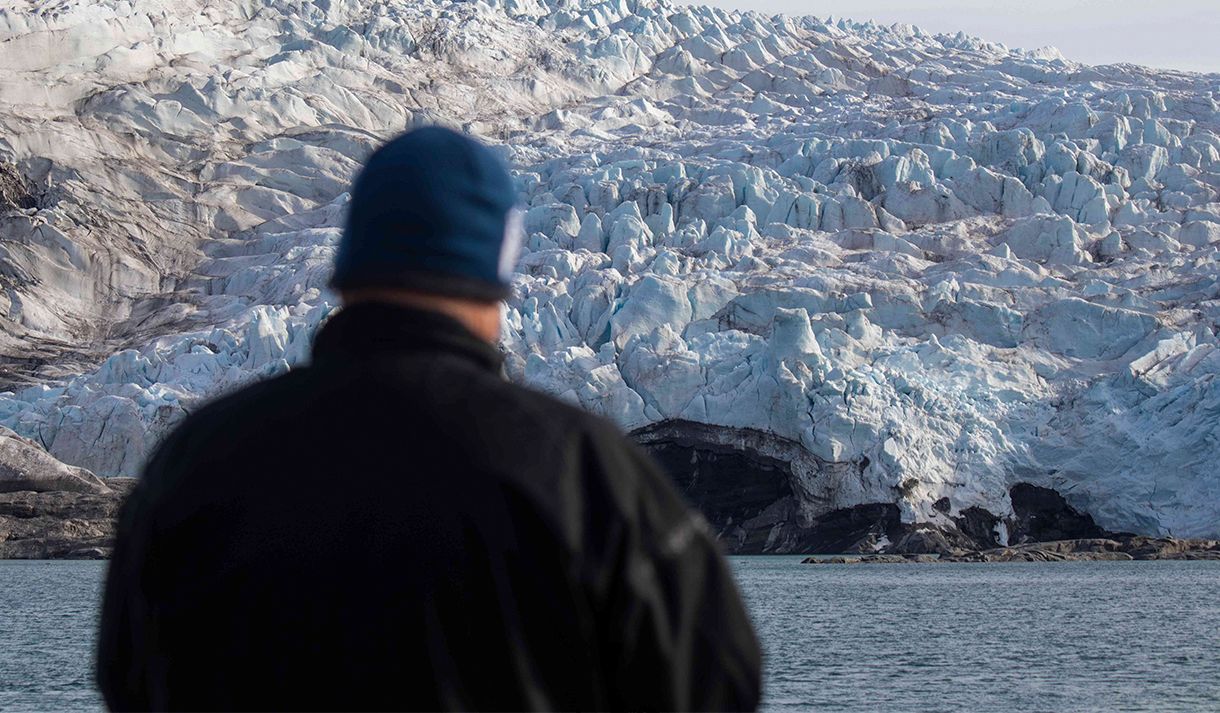 A guest standing on a boat in the foreground looking out at a glacier in the background