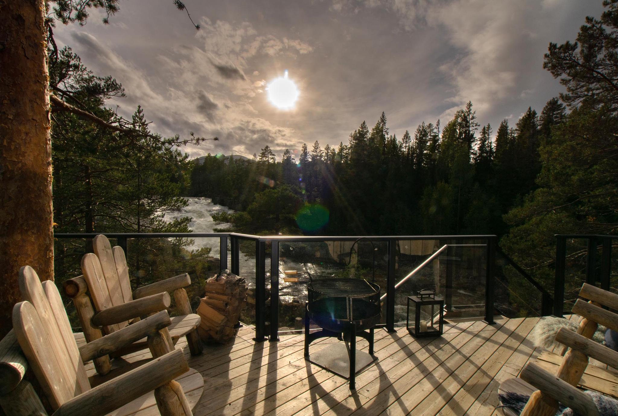 Wooden deck with solid wooden chairs with view to a waterfall against the sun 