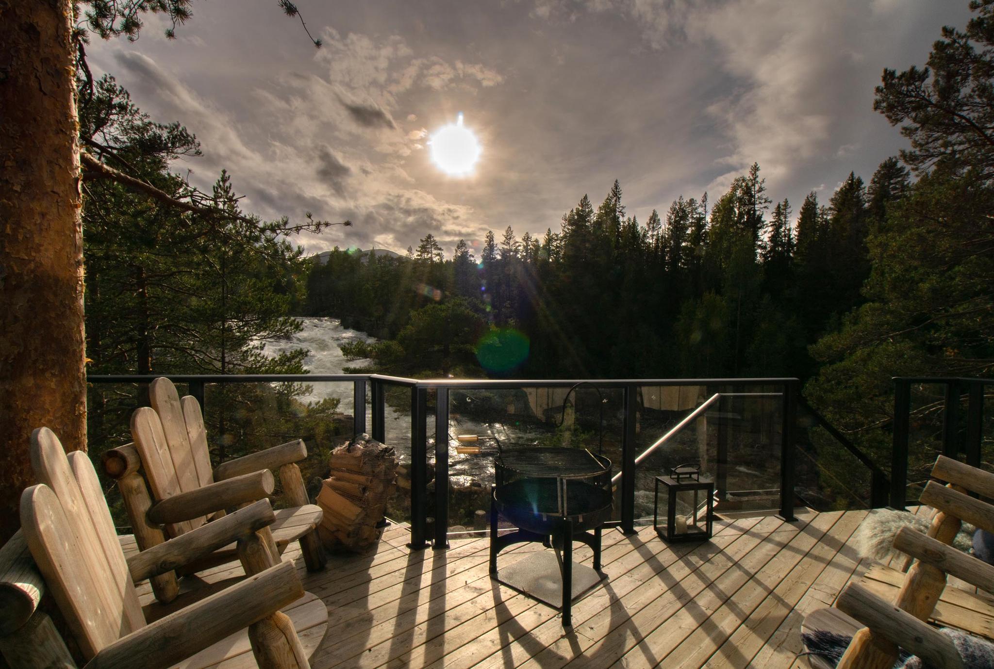 Wooden deck with solid wooden chairs with view to a waterfall against the sun