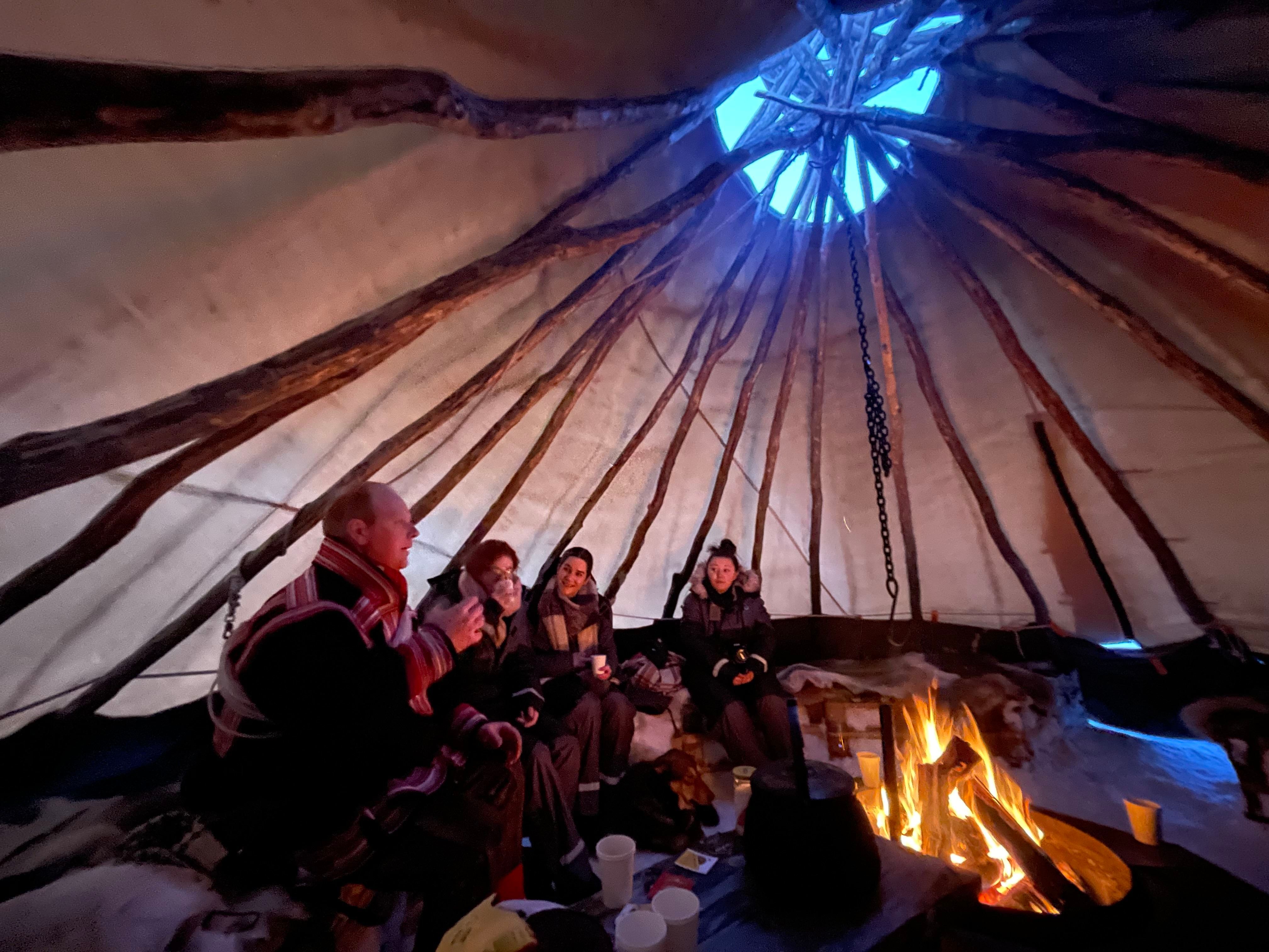People around a fire inside a traditional tent structure with an opening at the top