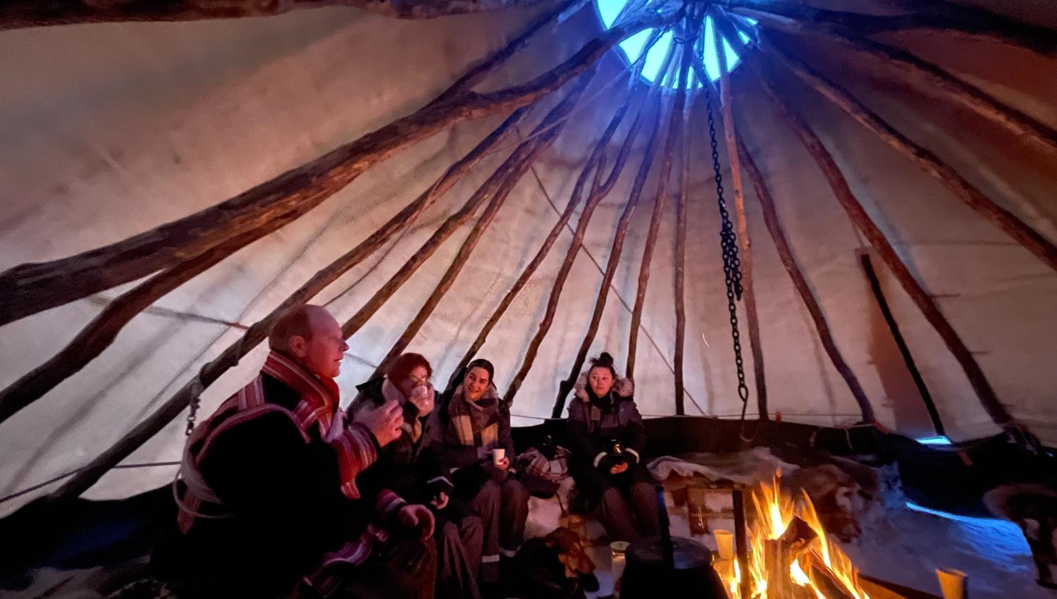 People around a fire inside a traditional tent structure with an opening at the top