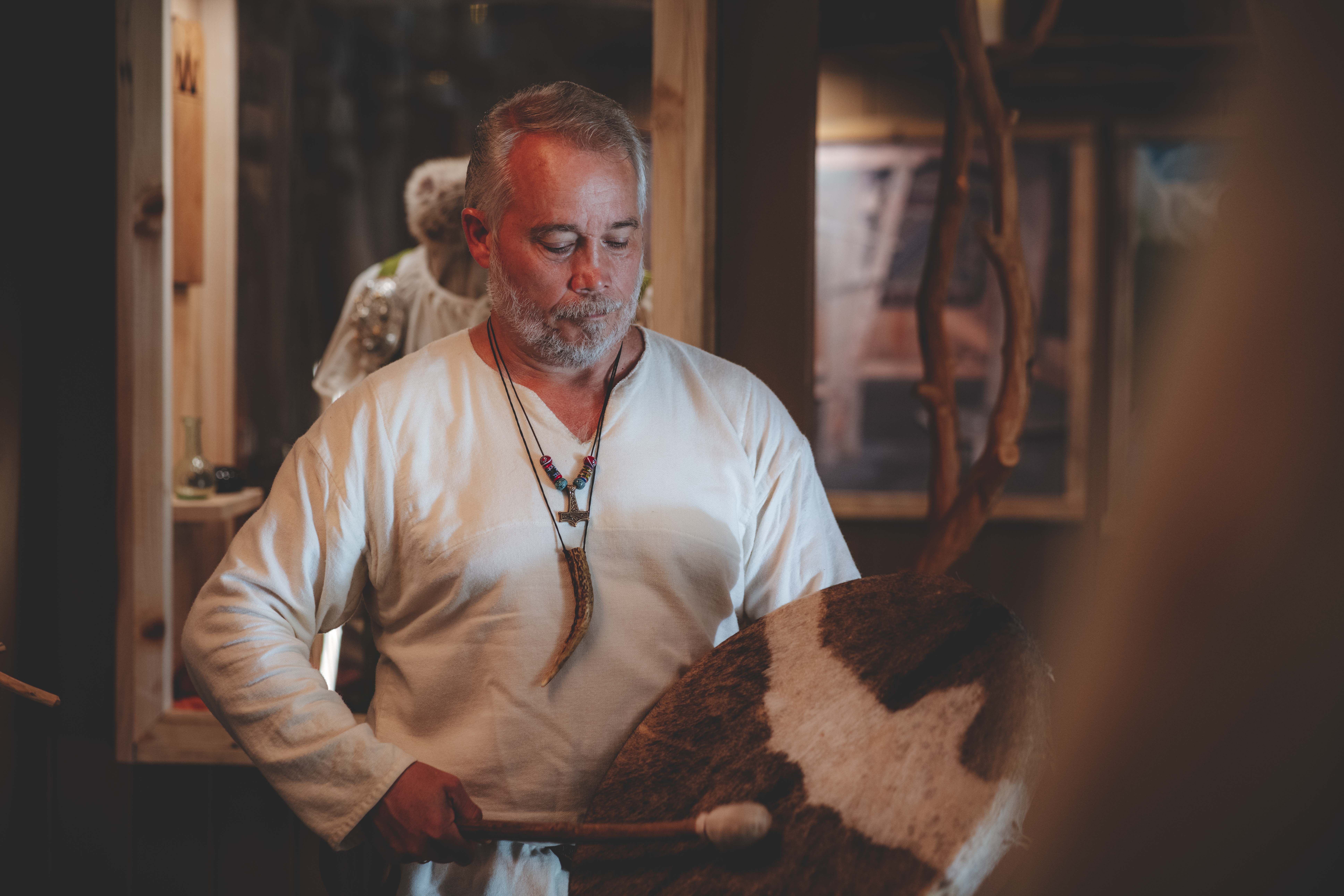 Ein Mann in Wikingerkleidung spielt in der Ausstellung eine Wikingertrommel.