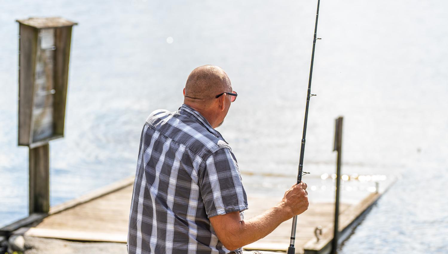 En mann som sitter og fisker ved båtutsettplassen