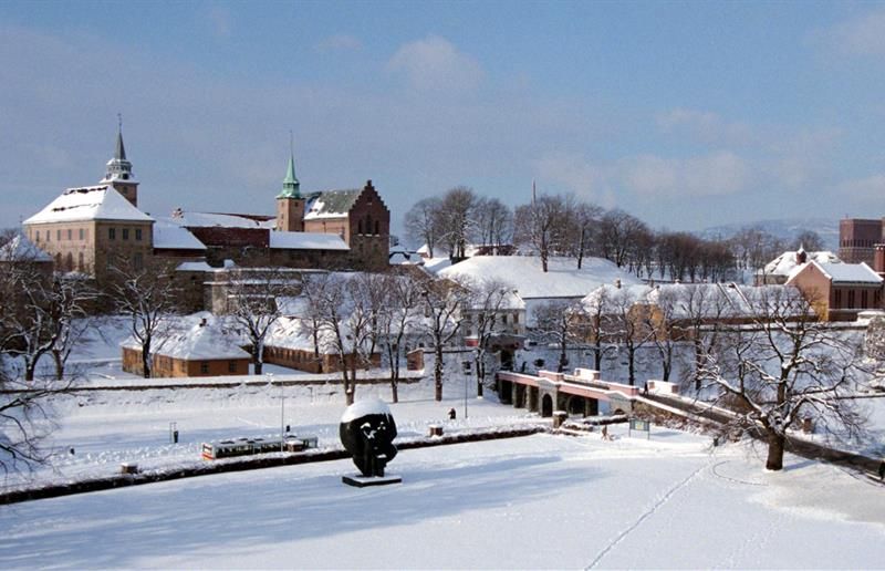 Winter photo of the fortress covered in snow, seen from afar. City Hall in the background on the right side.