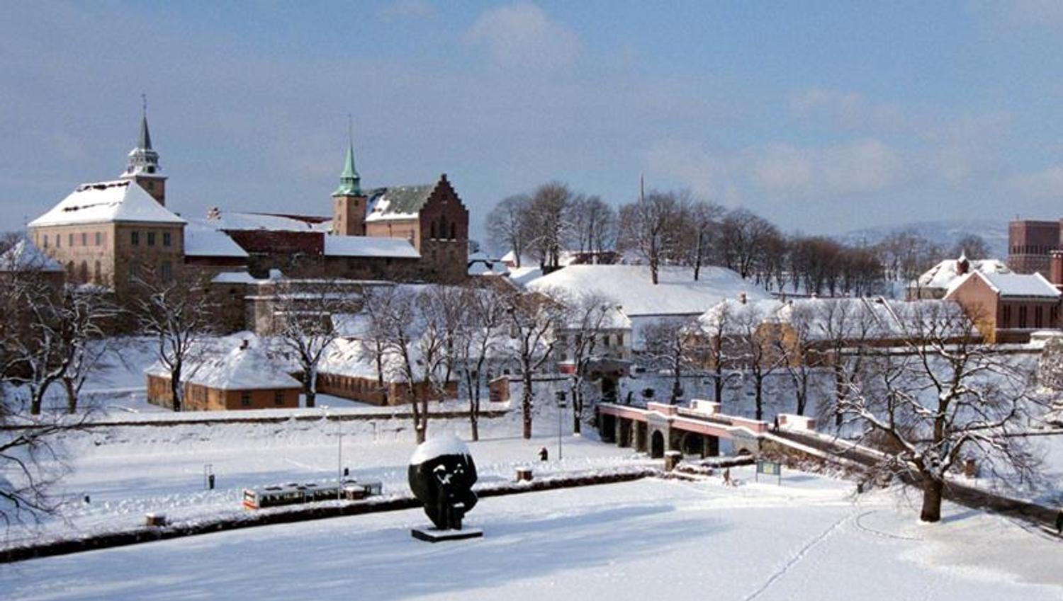 Winter photo of the fortress covered in snow, seen from afar. City Hall in the background on the right side.