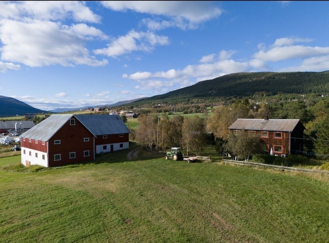 Aerial view of traditional farm buildings situated in an open valley with fields, trees, and mountains in the background under a clear sky.