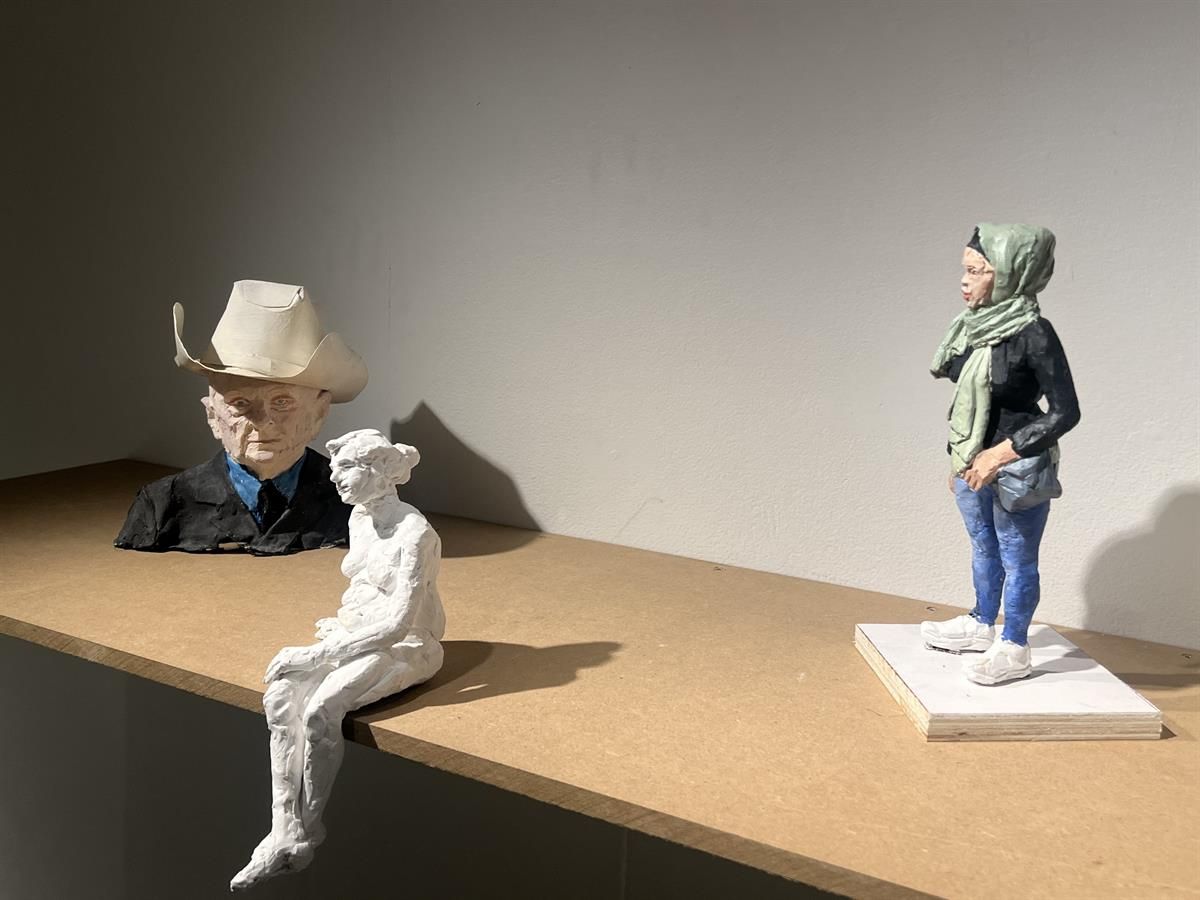 Sculptures of figures displayed on a wooden surface in a gallery.