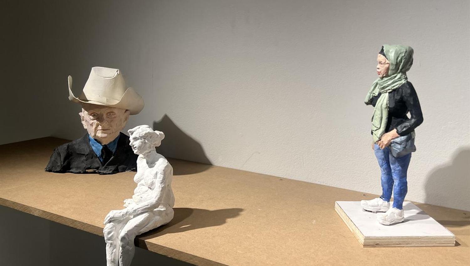 Sculptures of figures displayed on a wooden surface in a gallery.