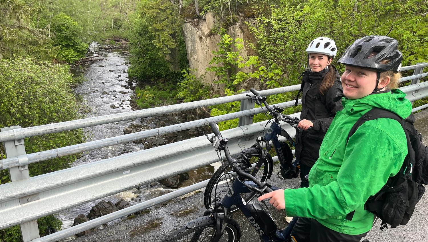 Syklistene står oppå brua og ser på elven