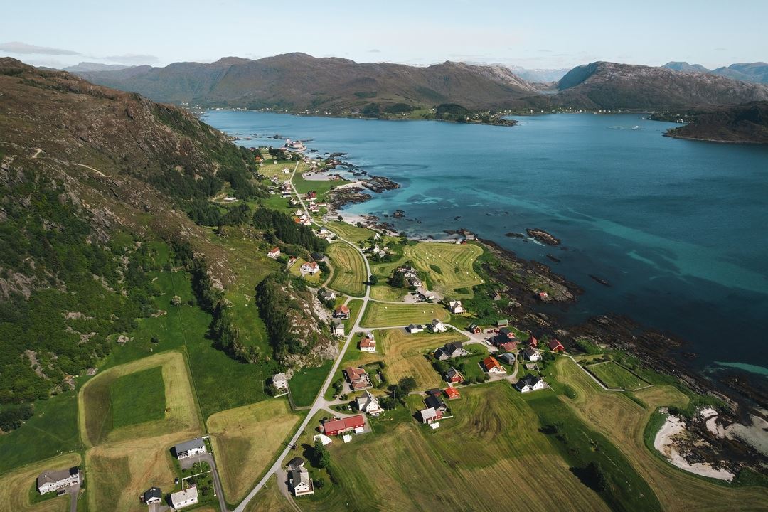 Dronefoto av Grotle og Iglandsvik.ved turkis hav, med fjell i bakgrunnen..