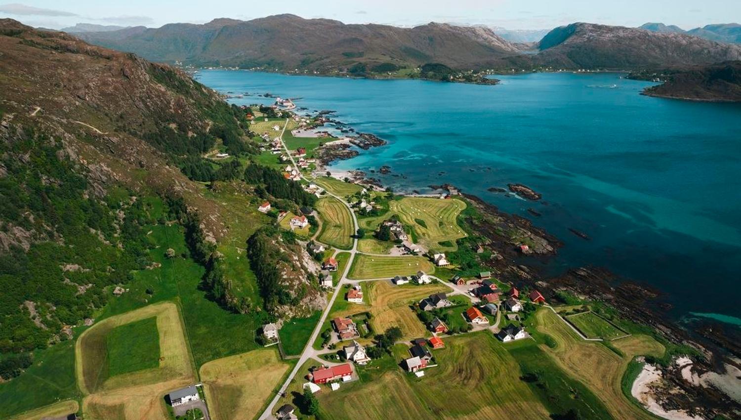 Dronefoto av Grotle og Iglandsvik.ved turkis hav, med fjell i bakgrunnen..