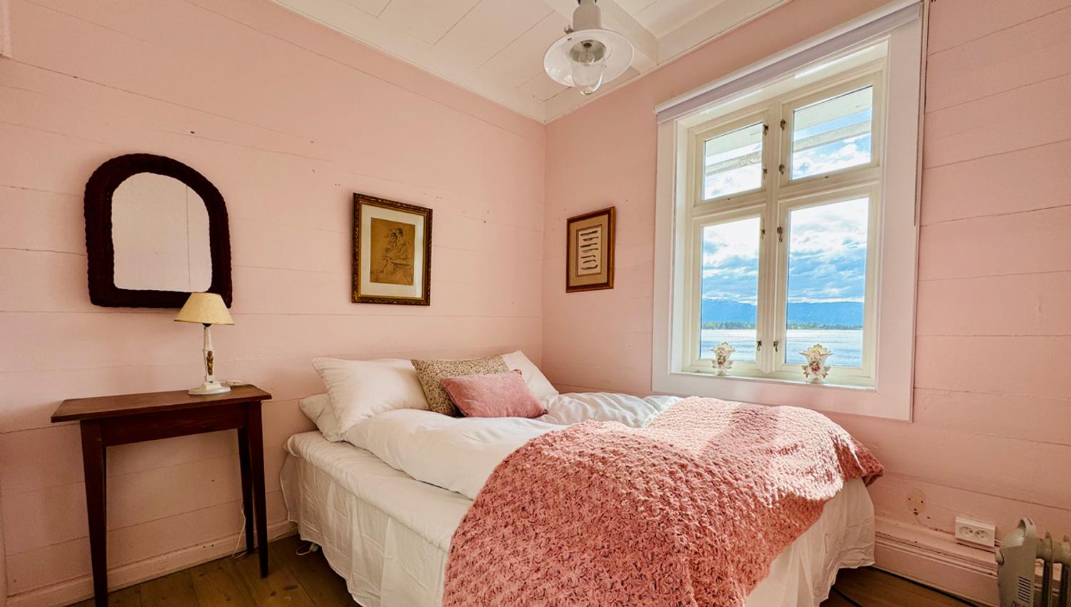 The Pink Room at Kramsjø Guesthouse, featuring soft pastel tones and a view towards the fjord.