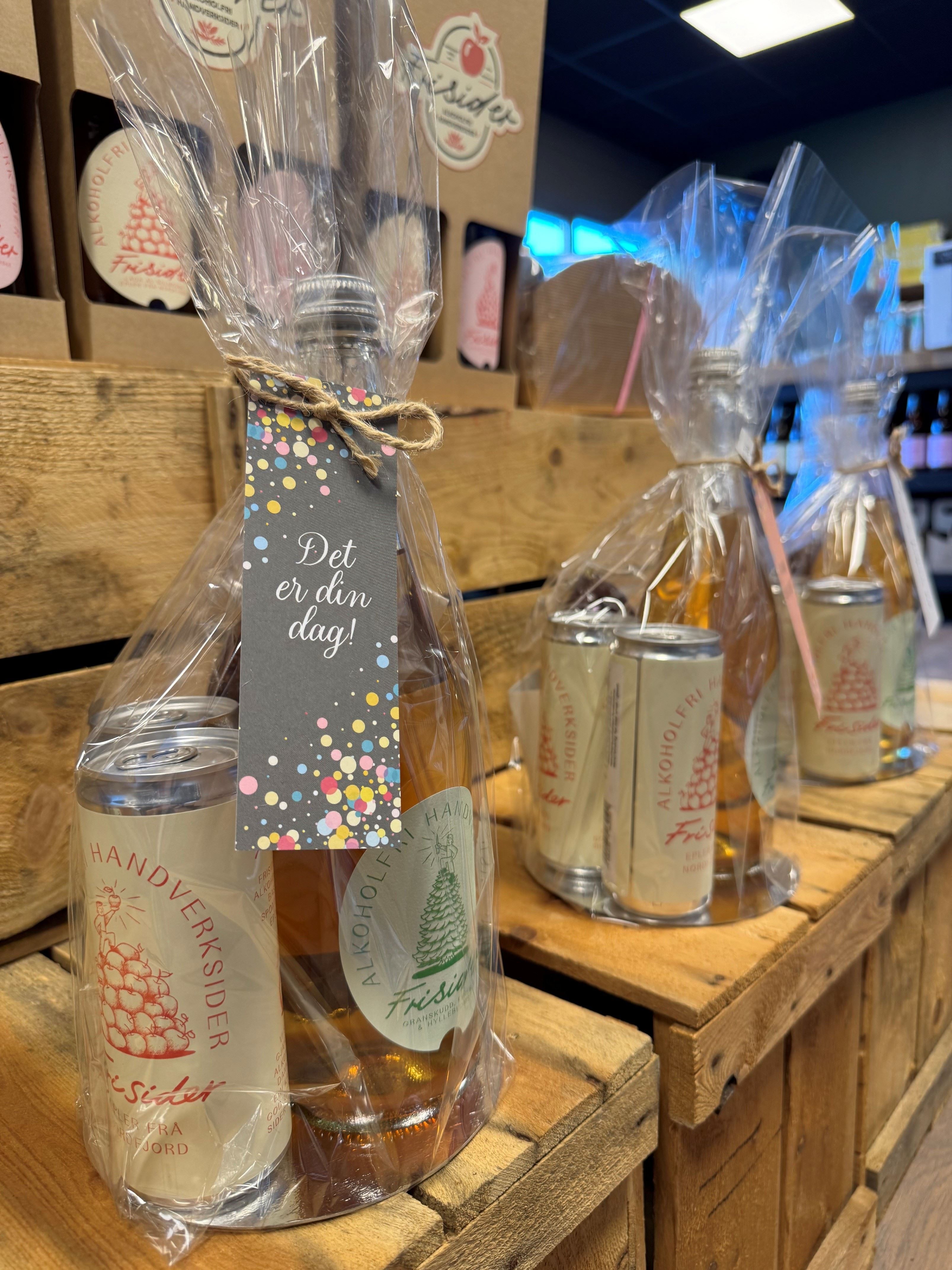 Cellophane-wrapped drink gift sets with a bottle and cans tied with twine, displayed on wooden crates in a shop.