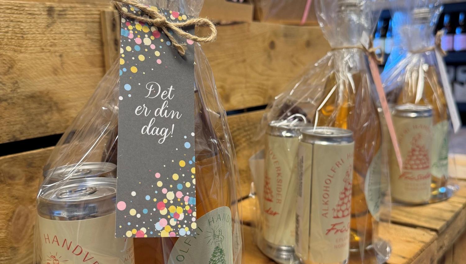 Cellophane-wrapped drink gift sets with a bottle and cans tied with twine, displayed on wooden crates in a shop.