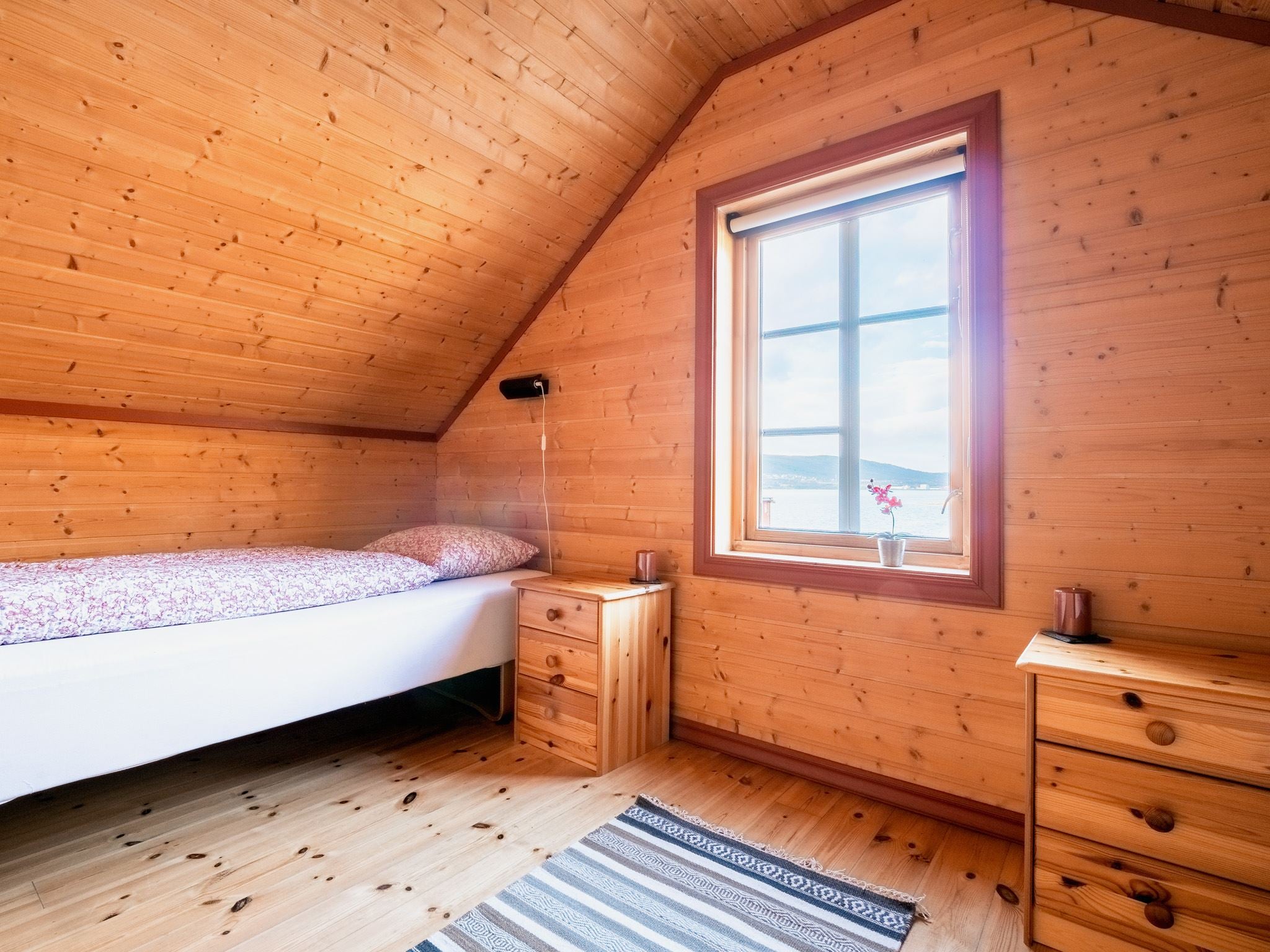 Bedroom with a slanted ceiling, bedside tables, and a window with a view and a plant on the sill