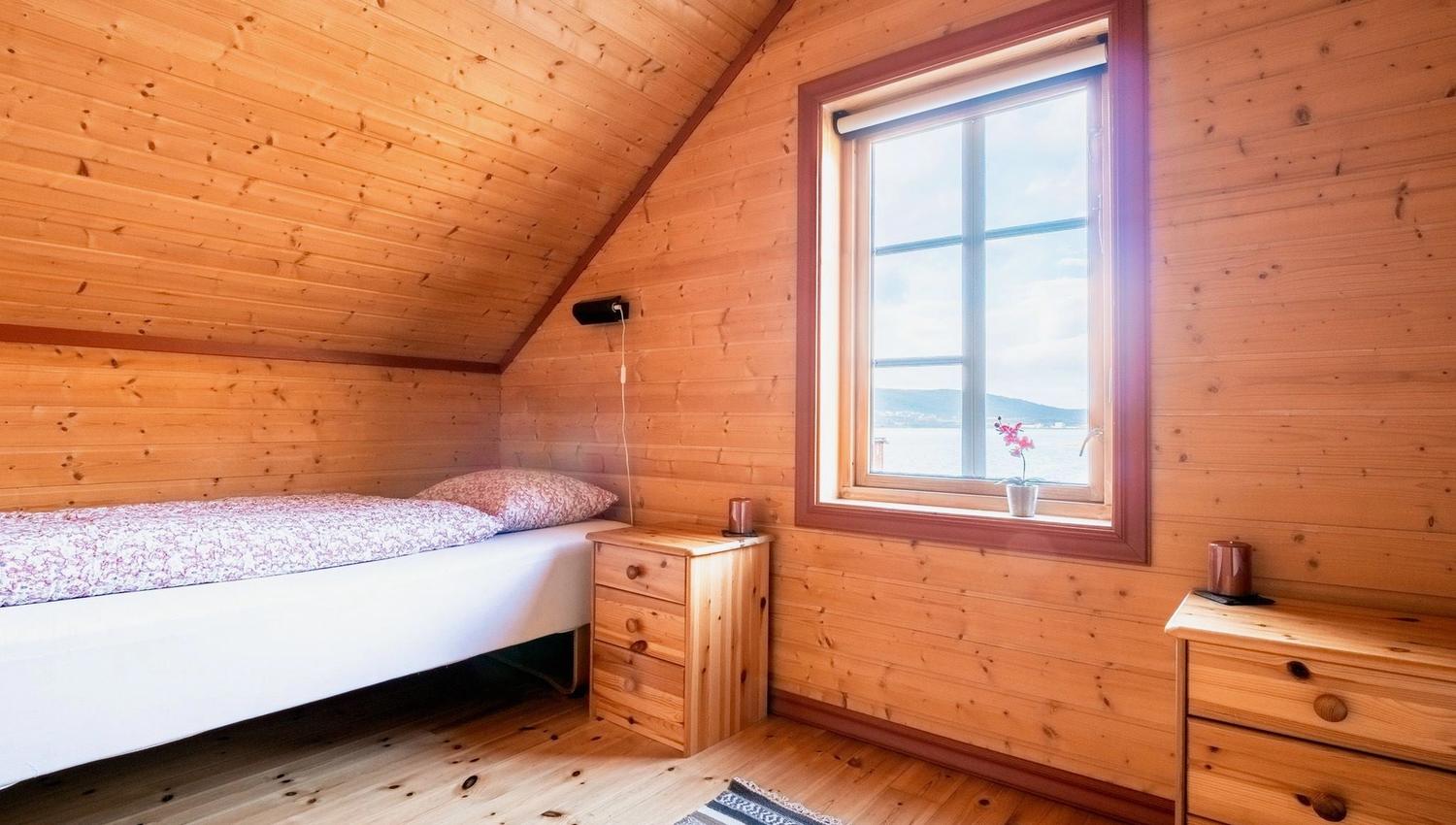 Bedroom with a slanted ceiling, bedside tables, and a window with a view and a plant on the sill