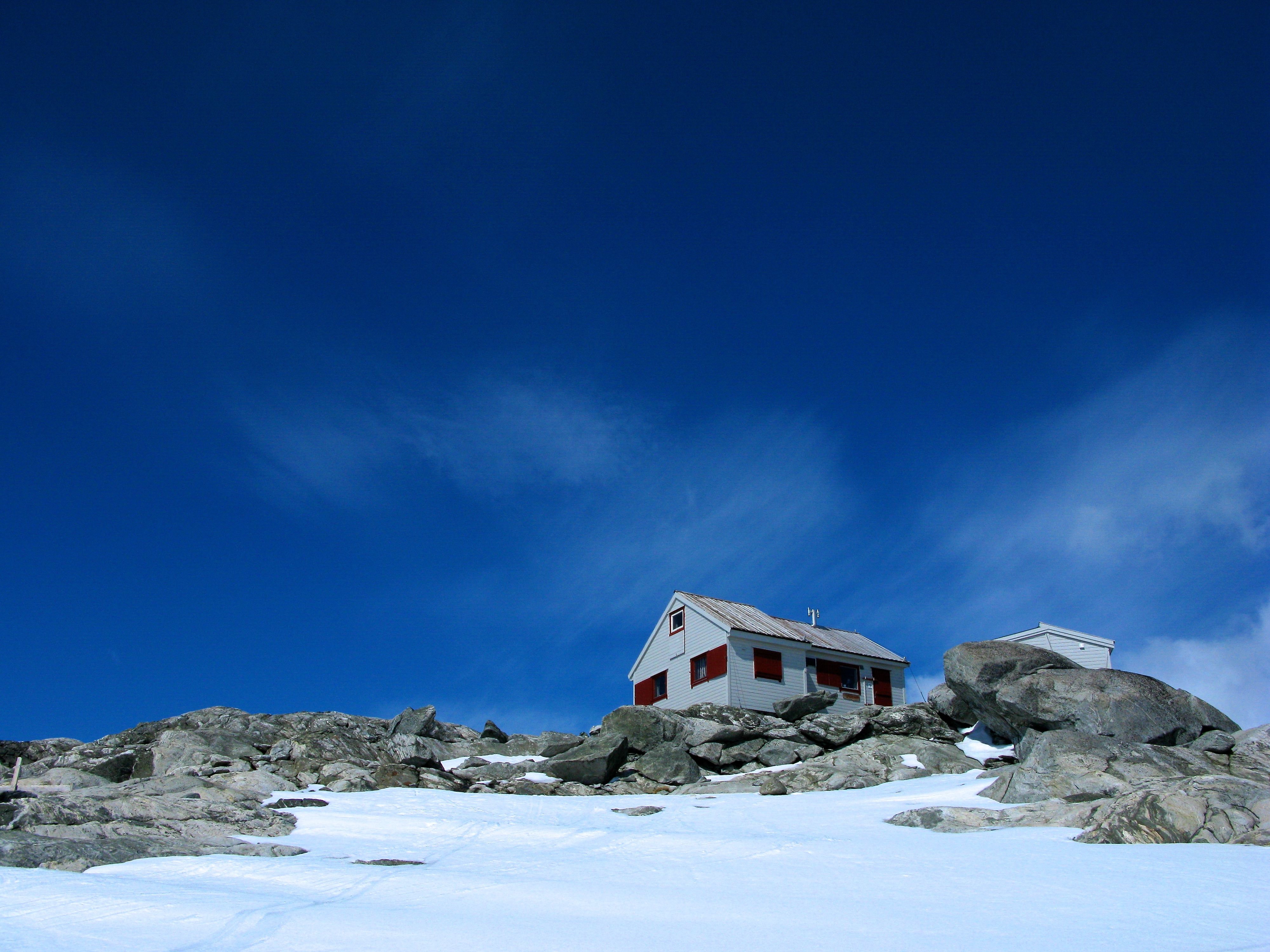 The Holmaskjer mountain cabin surrounded by snow and rocks beneath a deep blue sky.