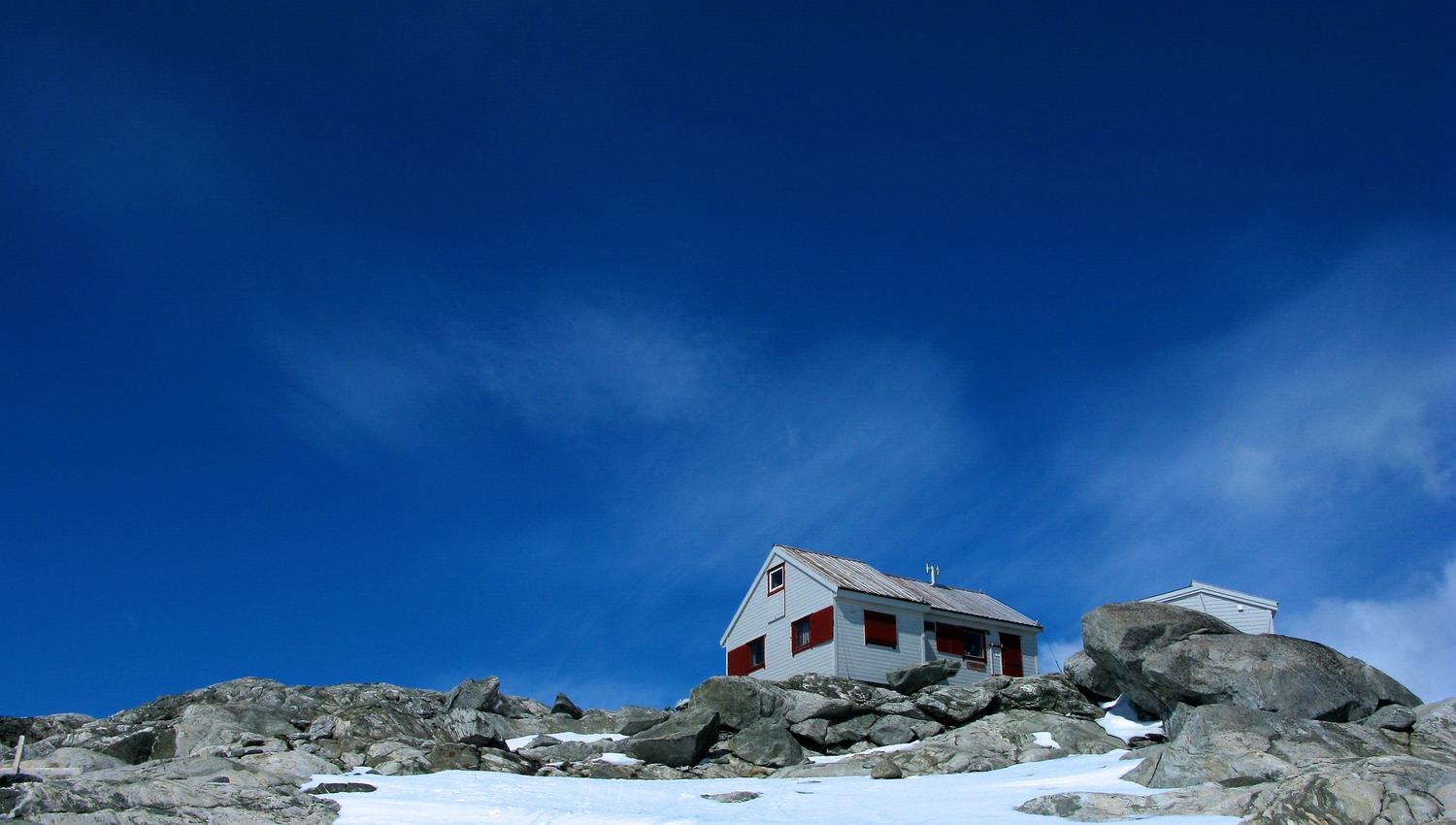 The Holmaskjer mountain cabin surrounded by snow and rocks beneath a deep blue sky.
