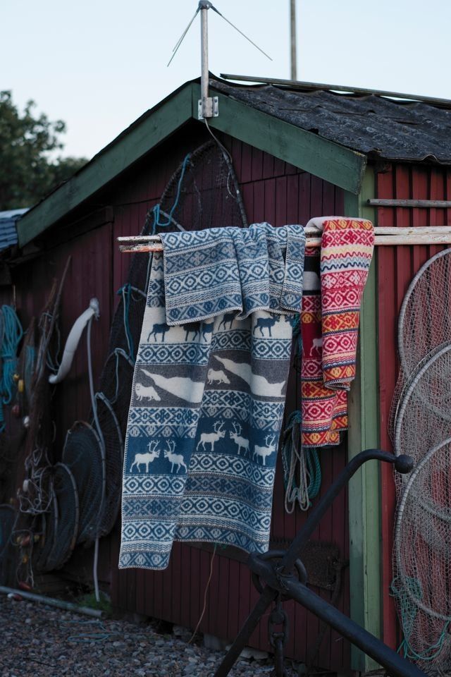 Blankets featuring traditional patterns hanging outside a boathouse.