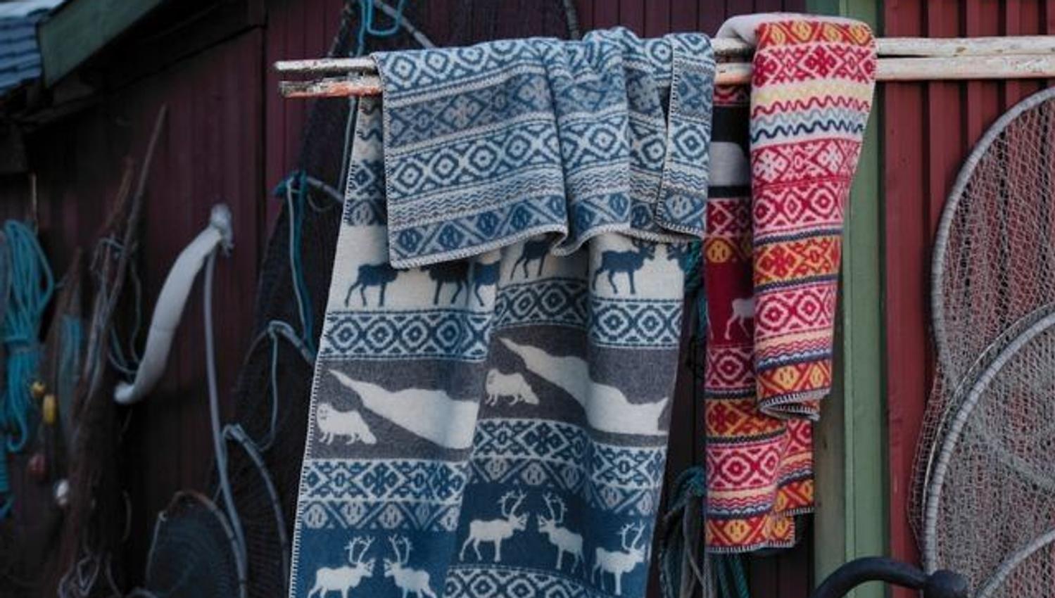 Blankets featuring traditional patterns hanging outside a boathouse.