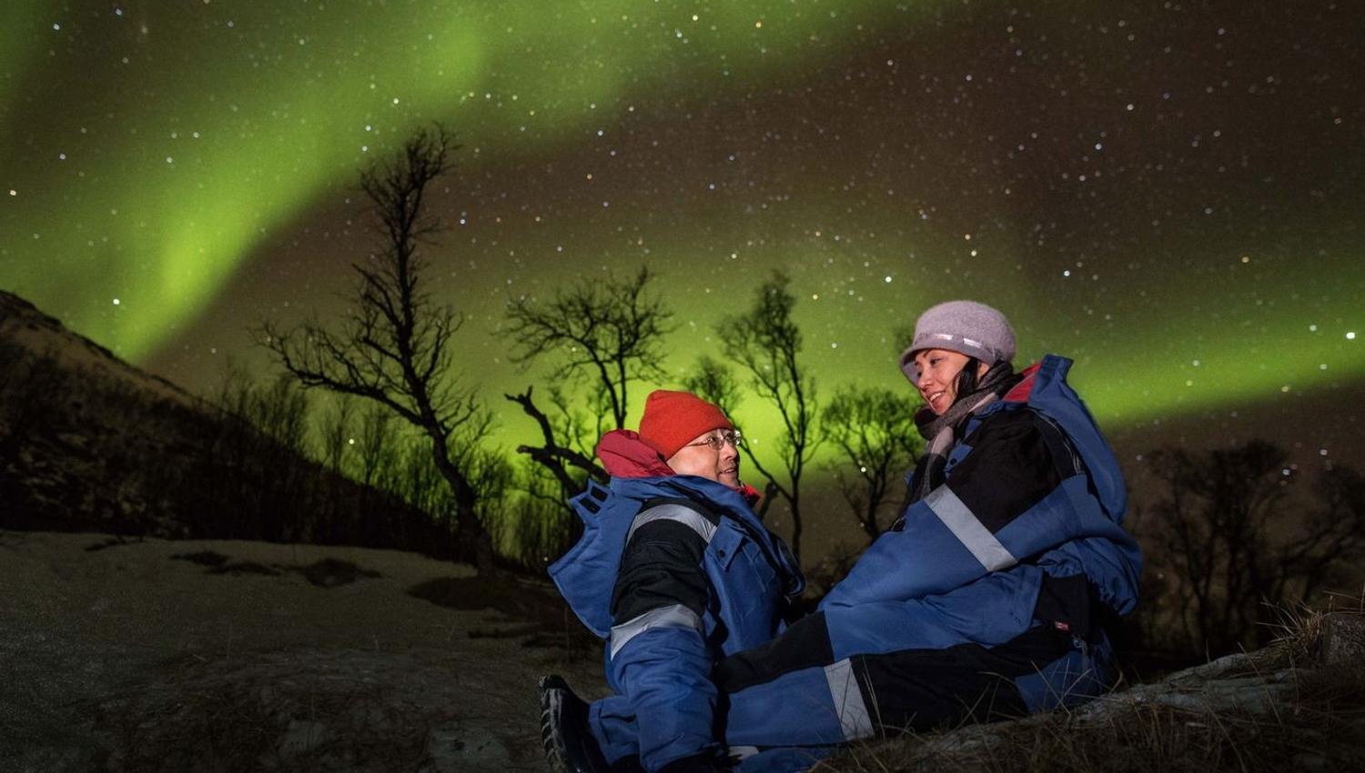 Two guests sitting under the northern lights