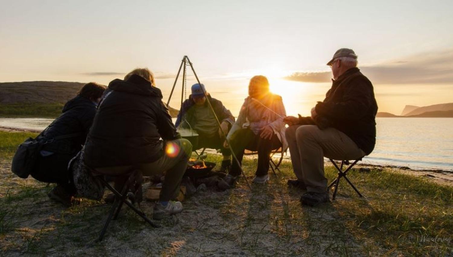 A group of guests sitting around a bonfire by the shoreline