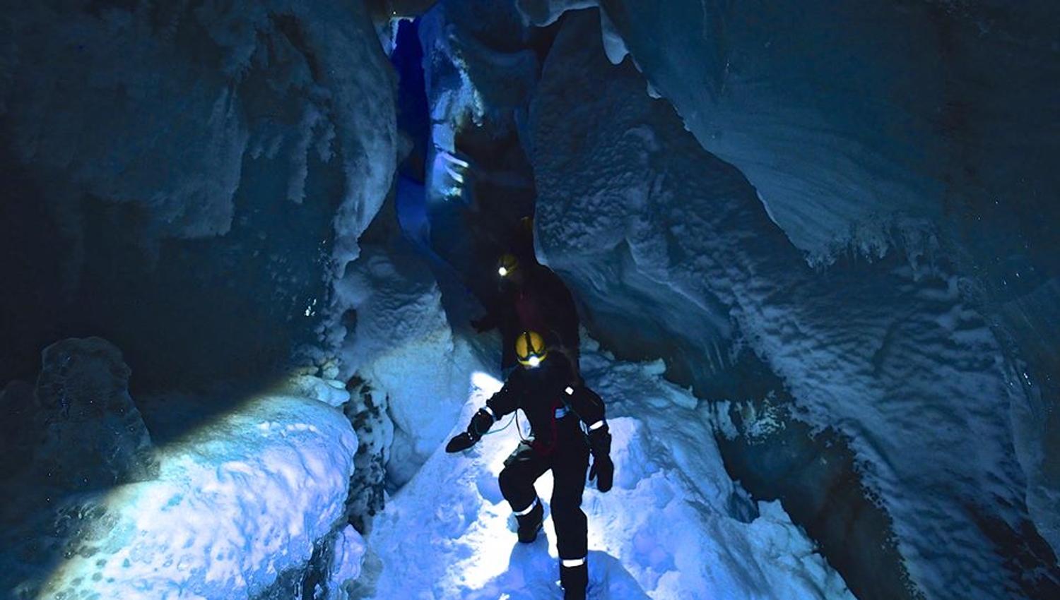 Persons inside the ice cave with headlamps on