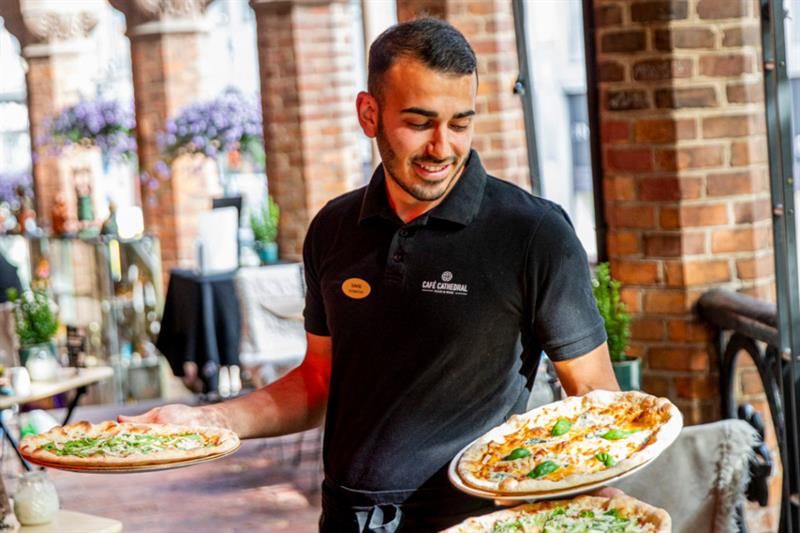 Waiter carrying three pizzas.