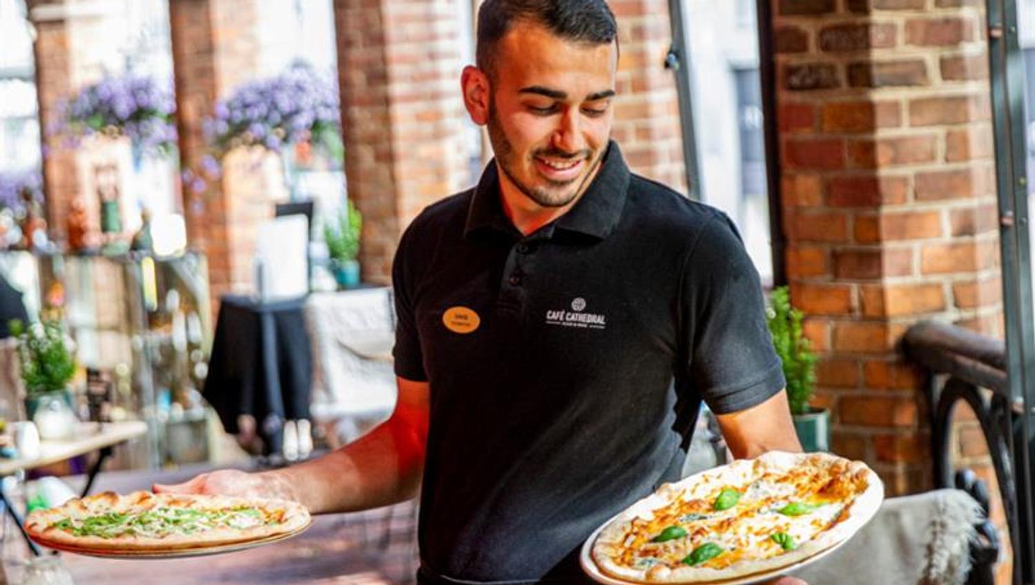 Waiter carrying three pizzas.