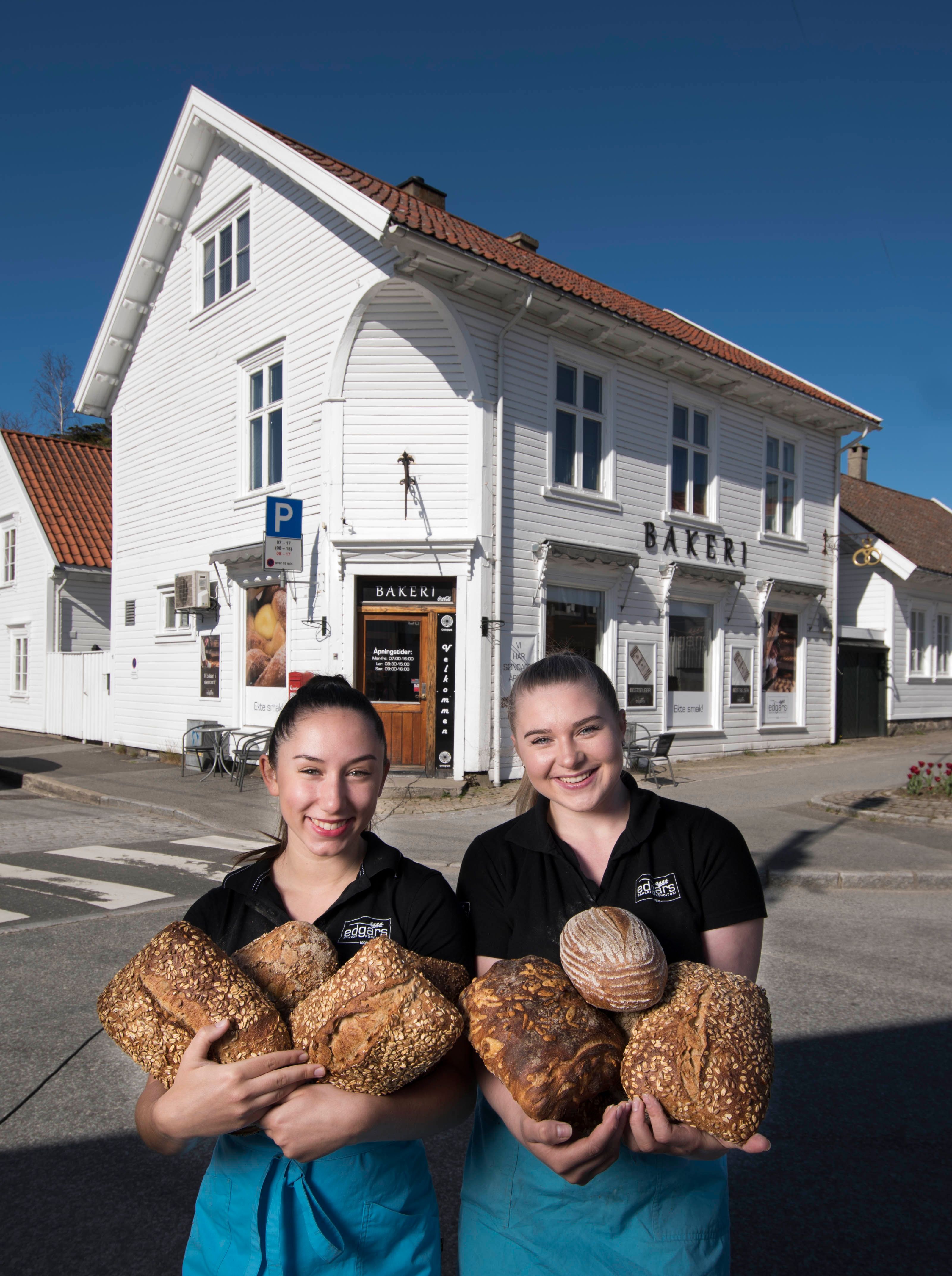 Two smiling girls with loaves of bread in their arms in front of the bakery.