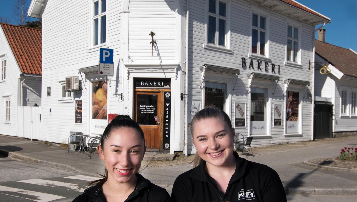 Two smiling girls with loaves of bread in their arms in front of the bakery.